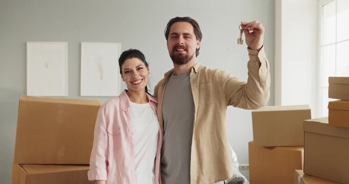 Couple homeowners holding keys amid moving boxes. Smiling man and woman unpacking in a new home after relocation. Clear concept of new home