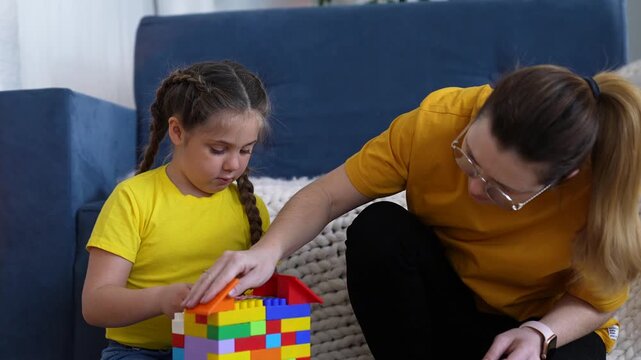 Mother and daughter play with block. They sit on floor at home. Child and mother construct house toy. Colorful building activity brings family together. Fun play with block creates strong bond.