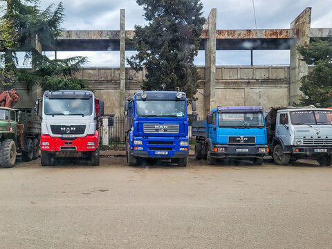A row of parked trucks, including MAN TGS, F2000, L2000, and KamAZ dump trucks, in a parking lot in front of an industrial facility in Kutaisi; commercial vehicles and freight transport; Georgia 5.425