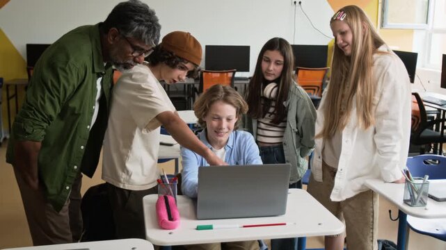 Caucasian teenagers and South Asian middle aged male teacher collaborating around laptop in classroom. Ideal for promoting STEM education, school technology, and collaborative learning software
