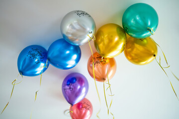 Fototapeta premium Colorful helium birthday balloons float near the ceiling with curling ribbons. Festive decoration creates a cheerful party and celebration atmosphere.