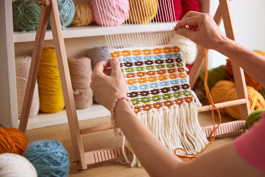 Woman weaving a colorful tapestry on a wooden frame loom using yarn, handmade textile craft