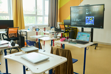 Naklejka premium Empty modern classroom featuring interactive smartboard and laptops on desks. Image represents STEM education and digital learning, ideal for school promotional materials