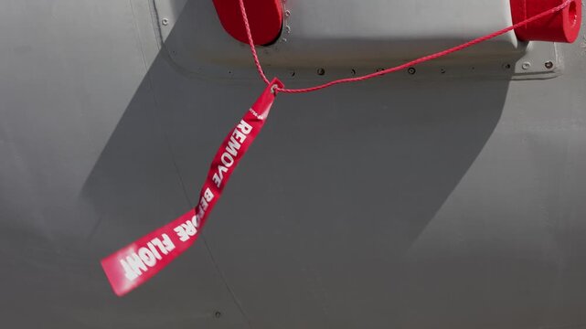Remove Before Flight &mdash; red safety warning ribbon and tag waving in the wind, attached to a grey airplane, plane and aeroplane. Aviation and aeronautics safety preflight procedure, check and control.
