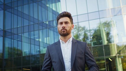 Fototapeta premium Confident businessman in a suit standing outside a modern glass office building