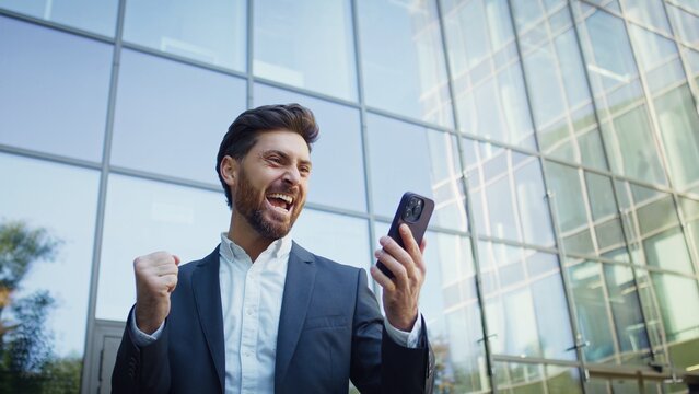 Excited businessman celebrating success while looking at his smartphone outside office building