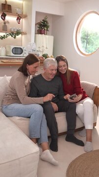The family&mdash;parents and middle-aged daughter&mdash;sit together on the sofa, holding smartphones to take selfies and chat while celebrating the Christmas holiday.
