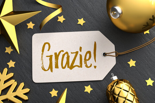 Christmas - Gift Tag with the Italian message "Grazie!" (Thanks!) on a black stone background with gold colored christmas ornaments around.