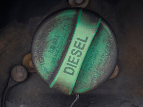 Close up of a dirty green diesel fuel tank cap labeled with instructions on a heavy vehicle outdoors