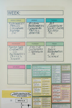 Vertical image of school weekly schedule poster with handwritten subjects hanging on wall next to coding cheat sheet, ideal for education and learning marketing campaigns
