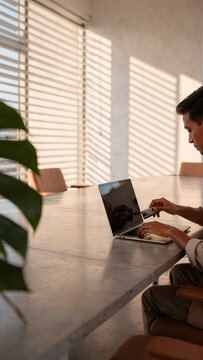 A man sits at a modern office table using a hardware security key and laptop illuminated by natural window light