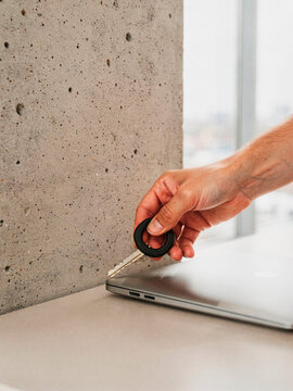 Close up of a man hand holding a key next to a closed laptop in a modern minimalist office environment