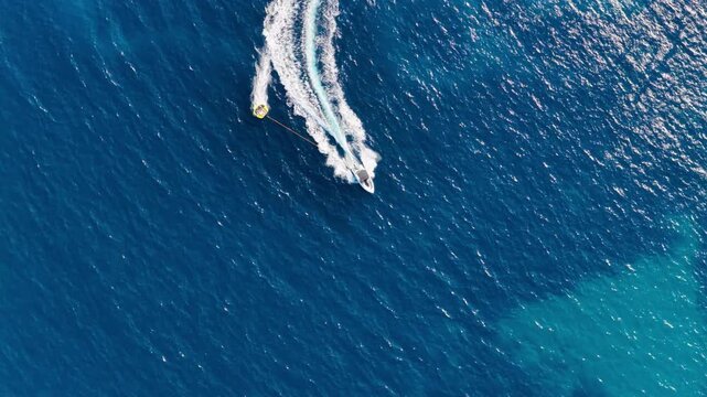 Aerial top down view of speedboat towing inflatable tube in blue sea, Paleokastritsa, Corfu island, Greece