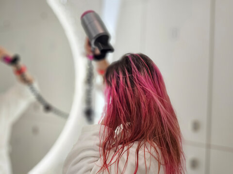 Girl with pink hair drying her hair in a bright room