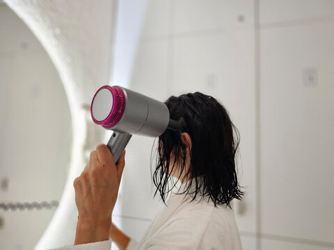 Woman using a hair dryer to dry her wet hair in a bathroom