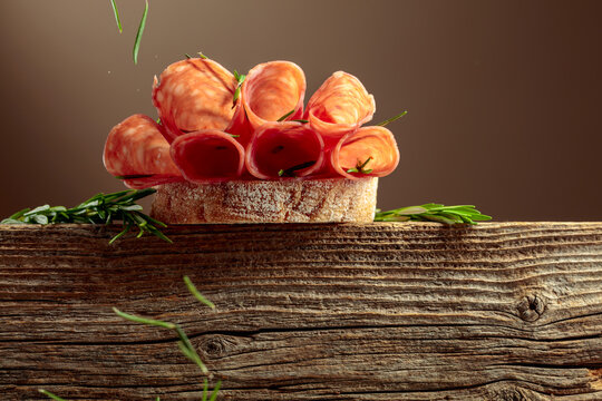 Sandwich with thin slices salami and rosemary on a wooden table.