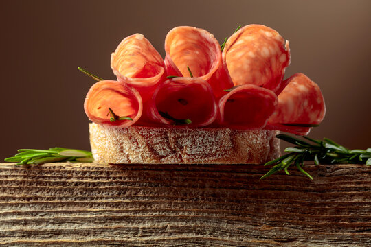Sandwich with thin slices salami and rosemary on a wooden table.
