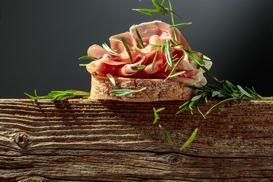 Sandwich with thin slices of Italian dry cured prosciutto, served on an old, weathered board.