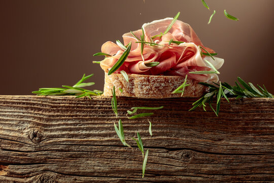 Sandwich with thin slices of Italian dry cured prosciutto, served on an old, weathered board.