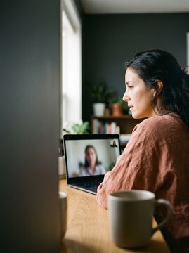 Focused young woman participating in a video conference call on a laptop from her cozy home office