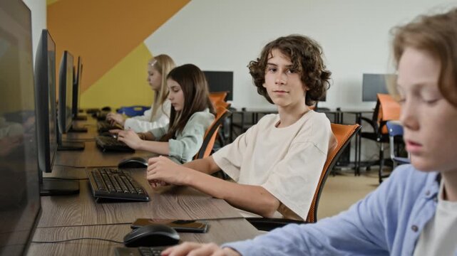 Portrait of Caucasian teenage boy looking at camera during computer science class with classmates. Perfect for marketing STEM education or school IT programs