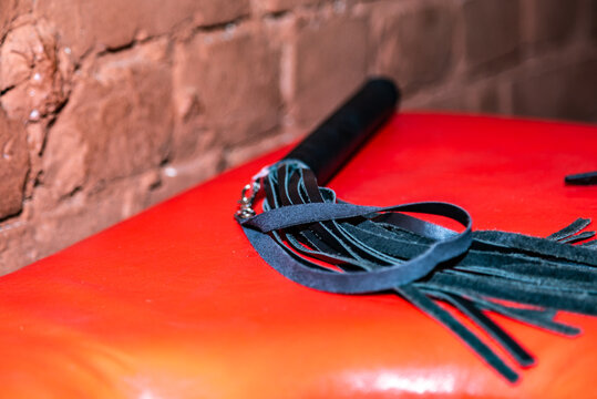 Dark leather flogger rests on bright red surface