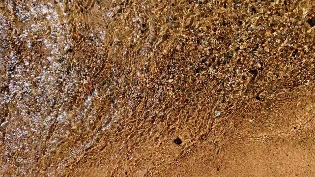 Sandy lakeshore with foamy shallow waves washing over wet pebbled sand creating natural texture