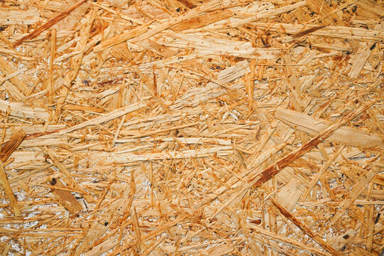 Close-up macro background of an oriented strand board (OSB) wooden panel showing compressed, interwoven wood chips and splinters with warm golden-brown tones.