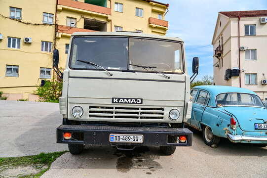 A gray KamAZ-5320 truck is parked next to a light blue GAZ-21 Volga classic car from the 1950s on a residential street in Sighnaghi; historic Soviet vehicles, Kakheti region, Sighnaghi, Georgia 12.4.2