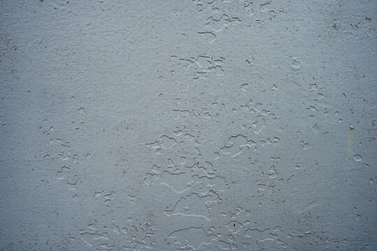 Detailed texture of a flat light-grey painted surface showing subtle cracking, peeling chips, and slight metal oxidation underneath.