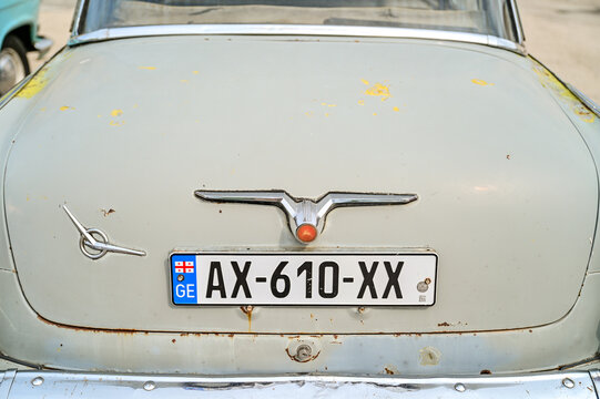 Rear view of a grey GAZ-21 Volga classic car with a Georgian license plate and a chrome handle emblem; close-up of weathered paint and rust on a historic vehicle in Sighnaghi, Georgia