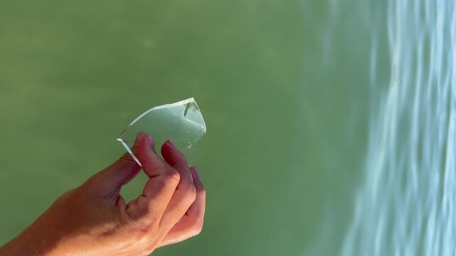 Female hand holding a piece of glass found on the seabed in shallow seawater. 4k