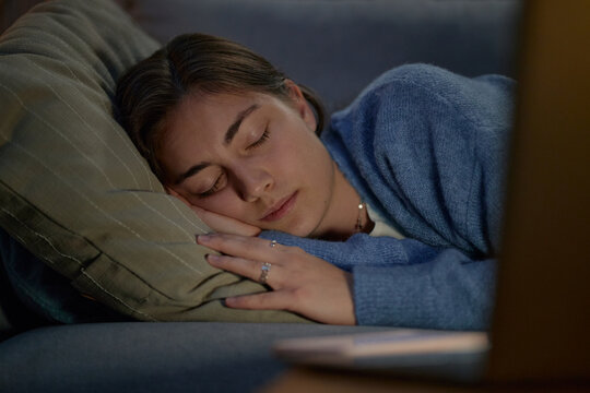 Caucasian young adult woman sleeping on sofa next to open laptop, exhausted from overworking, representing burnout and fatigue, suitable for mental health awareness campaigns