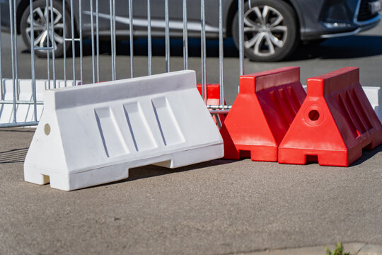 Red and white plastic water-filled traffic barriers and galvanized steel crowd control barricades arranged for temporary urban safety
