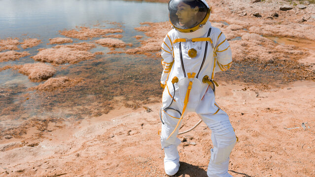 Woman astronaut in white spacesuit exploring red alien planet shore in dynamic pose