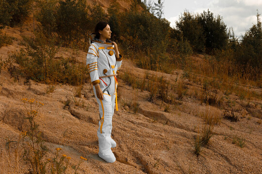 Thoughtful woman astronaut holding helmet on sunlit hillside with autumn nature