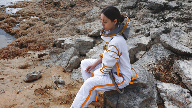Tired astronaut resting on a rock after a long expedition on an alien coast