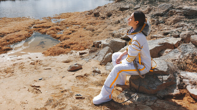Female explorer sitting on a stone and looking up at the sky of a distant world
