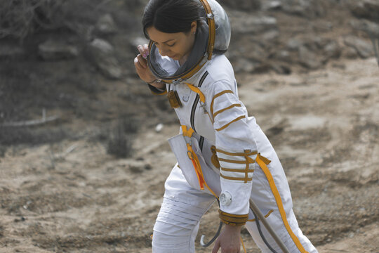 Astronaut examining a tiny sample held between her fingers on a barren planet