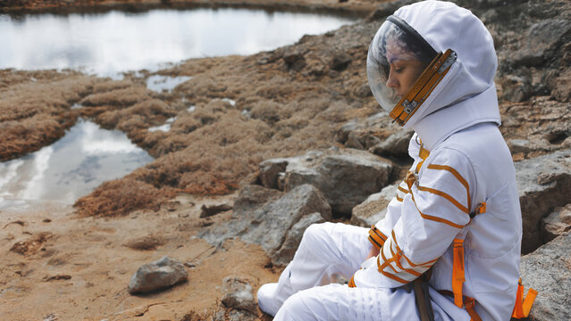 Astronaut in a glass helmet sitting beside a still lake with space for text