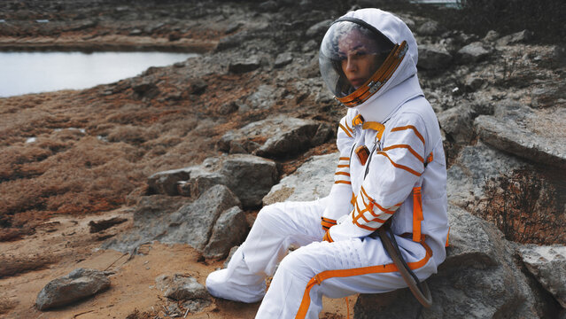 Sci fi poster scene of a seated astronaut in a closed helmet on a barren shore