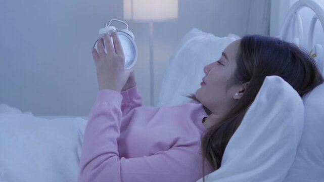 Sleep and waking concept, tired woman checking alarm clock while lying in bed at night, struggling to wake up, sleep routine, alarm clock, tiredness, insomnia, morning routine