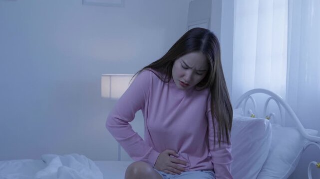 Abdominal pain concept, woman holding stomach while sitting on bed at home, suffering cramps and discomfort, abdominal pain, menstrual cramps, stomachache, food poisoning, illness