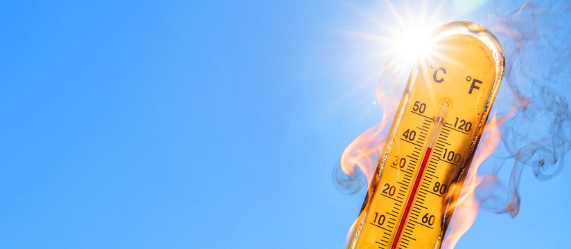 A thermometer engulfed in flames, showing a high temperature against a blue sky, with space for text. Extreme heat. A concept representing global warming, climate change, and weather conditions
