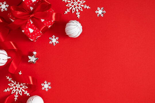 Christmas Frame Composition With Red Gift Box, White Snowflakes, Baubles and Silk Ribbon On Red Background. Festive Winter Holiday Flat Lay Layout With Copyspace For Text, Banner Or Greeting Card
