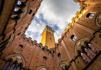 Fototapeta premium Blick durch eine enge Gasse auf den Torre del Mangia, den markanten Glockenturm des Palazzo Pubblico in Siena, Toskana, Italien