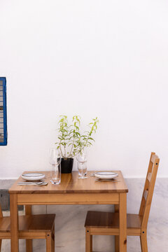 minimal shot of wood table set for two with dishes, glasses, and florals, against whitewashed wall in europe 