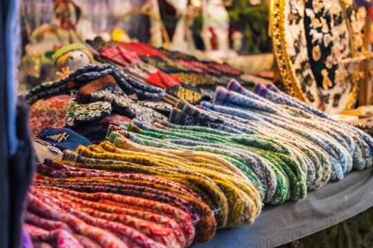 Woven textile variety spreads across a market table in rows of colorful patterned garments, showing skilled handmade production in Riga for local craft, winter fashion and gift stories.