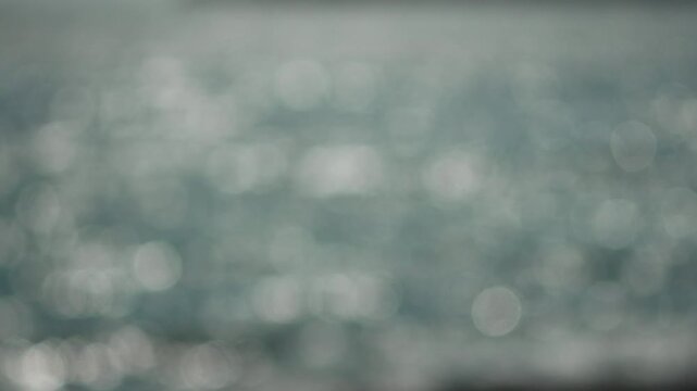 Abstract bokeh background displays dancing light patterns upon ripples of moving blue water outdoors. Soft focus aesthetic shot.