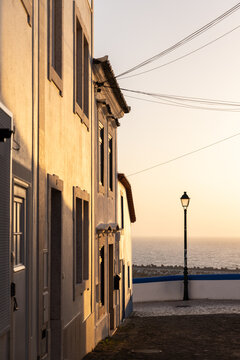 view from narrow residential cobblestone street in Ericeira, Portugal looking towards ocean during golden hour